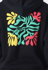 Sudadera negra con una gran gráfica en la parte posterior que presenta patrones en relieve coloridos en verde, rojo y amarillo. Texto incluido en el centro.