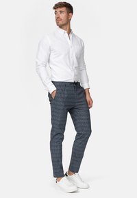 Chemise blanche à boutons, associée à un pantalon à carreaux bleu marine, avec une taille élastique et des baskets blanches, sur un fond clair.