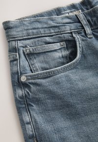 Hele sinine teksapüksid keskmise taljega, õrnalt kulunud, tavaliste taskutega ja nööpdetailiga esimesel taskul.