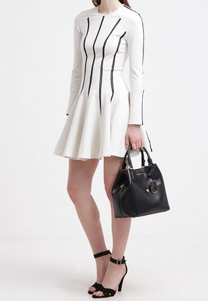 Bílé dlouhé šaty s dlouhým rukávem a rozšířenou sukní, s černými vertikálními pruhy; černá kabelka s detaily; černé sandály na podpatku se stříhacími pásky. Hladká struktura látky.