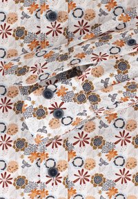 White fabric shirt featuring a colorful floral pattern in orange, red, and navy, with dark buttons and a buttoned cuff detail.