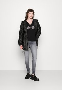 Svart, teksturert jakke med hette, kombinert med en svart t-skjorte med sølvglitter, lysegrå smale jeans og svarte platå sko.