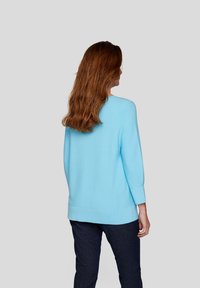 Helles blaues Sweatshirt mit rundem Ausschnitt und langen Ärmeln, aus einem glatten Material gefertigt, kombiniert mit dunklen Jeans.