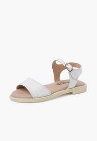 White leather sandal featuring a wide toe strap, ankle strap with silver buckle, and beige insole. Flat sole with a slight textured grip.