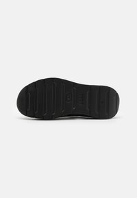 Semelle de chaussure en caoutchouc noir avec de profondes rainures horizontales et texte embossé "BOSS" et "38" visible sur fond blanc.