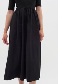 Schwarzes Baumwoll-Midikleid mit tailliertem Oberteil und gerafftem Bund. Glatte Textur mit Kellerfalten und einem fließenden Schnitt.