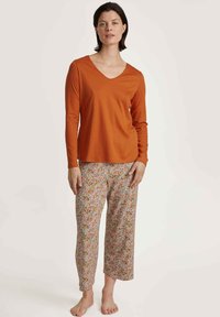 Oranje lange mouw V-hals top gecombineerd met loszittende, gebloemde, lichtgekleurde broeken. Zachte stof met een comfortabele pasvorm.