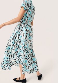 Květinové maxi šaty z lehké látky. Modro-černé abstraktní vzory na bílém pozadí. Rukávy a lem s volány. Černé baleríny s přezkami.