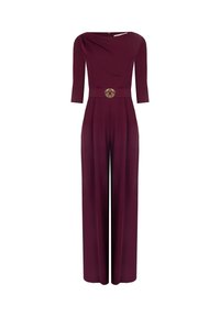 Tuta bordeaux con scollatura a barca, maniche a tre quarti e pantaloni a gamba larga. Presenta un'accento dorato a forma di cerchio in vita.