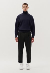 Granatowy sweter z golfem, luźny krój, prążkowany kołnierz. Czarne spodnie plisowane, z mankietami przy kostkach. Białe sneakersy dopełniają stylizację.