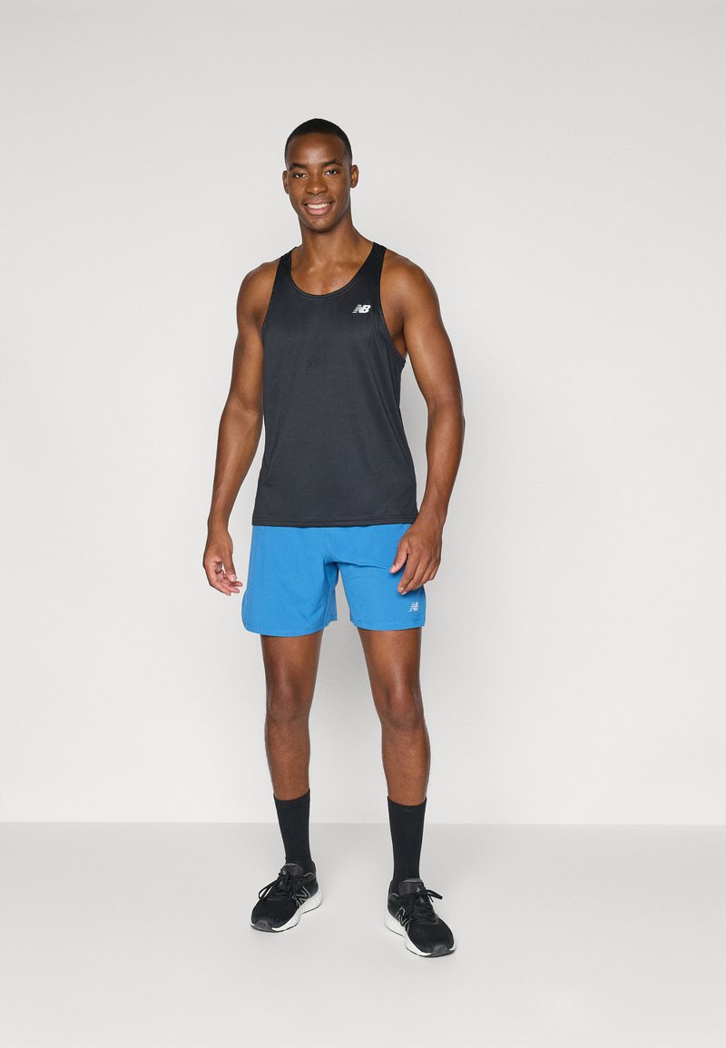 Schwarzes Sporttanktop und blaue Shorts, aus leichtem Stoff gefertigt. Verfügt über ein Logo auf dem Tanktop und hat eine normale Passform. Schwarze Sneaker und Socken.