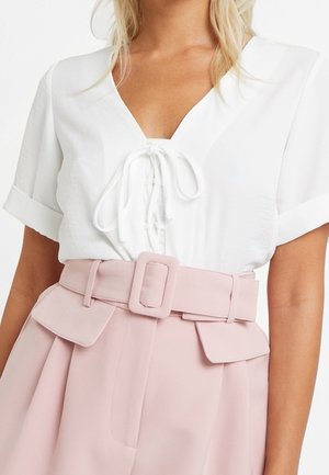 Haut blanc à manches courtes avec un profond décolleté en V et un détail noué à l'avant, associé à un pantalon rose taille haute avec une ceinture à la taille et des poches à rabat.