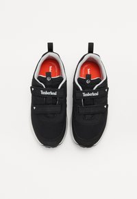 Crne tenisice izrađene od mrežaste i sintetičke tkanine, s čičak trakama, bijelim detaljima i crvenom unutrašnjošću s Timberland brandingom.
