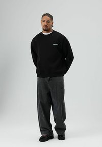 Sweat-shirt noir surdimensionné avec logo blanc, jean gris ample, et chaussures noires. Tissu lisse, design décontracté, silhouette droite.