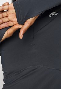 Persona che indossa una maglietta sportiva a maniche lunghe nera di Adidas con foro per il pollice, con la mano che spunta dalla manica.
