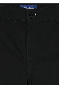 Pantalons en tissu noir avec une texture lisse, dotés d'une fermeture à bouton, d'une fermeture éclair cachée et de coutures contrastées au niveau de la taille.