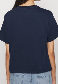 Námořnická modrá bavlněná tričko s krátkým rukávem, kulatým výstřihem a volným střihem. Výrazné švy podél ramene a zadního švu.