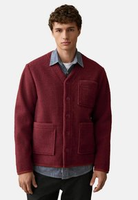 Burgunderfarbene Fleecejacke mit V-Ausschnitt, Knopfverschluss, zwei Vorderstaschen und einem kontrastierenden Jeanshemd darunter für zusätzliche Textur.