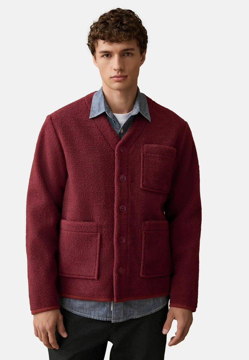 Burgunderfarbene Fleecejacke mit V-Ausschnitt, Knopfverschluss, zwei Vorderstaschen und einem kontrastierenden Jeanshemd darunter für zusätzliche Textur.