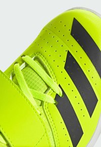 Scarpa sportiva neon gialla brillante con accenti neri, realizzata in materiale testurizzato, con perforazioni e un sistema di allacciatura prominente.