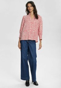 Camicia a bottoni floreale rossa e bianca, con maniche lunghe e scollatura a V, abbinata a jeans in denim a gamba larga e stivaletti neri.