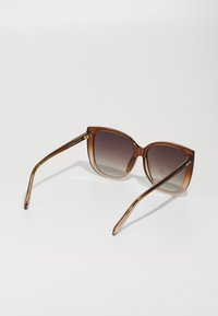 Braune Gradient-Sonnenbrille mit kantigen Rahmen und schlanken, goldakzentuierten Bügeln. Transparente braune Oberfläche mit glatter Textur.