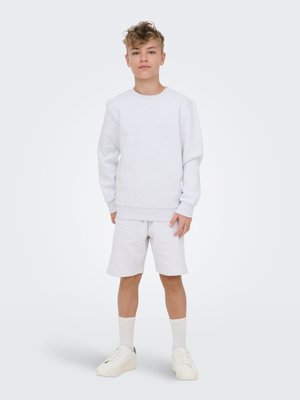 Boy stands facing forward wearing a white long-sleeve sweatshirt, matching shorts, white socks, and white sneakers on a plain light background.