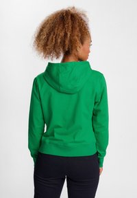 Zielona hoodie o dopasowanym kroju, z regulowanym kapturem i prążkowanymi mankietami. Tył wyróżnia się gładką teksturą i długością do talii.