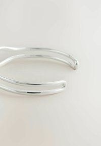 Bracciale a manchetto in argento con una finitura liscia e lucida, caratterizzato da un design minimalista e due bande curve intrecciate.