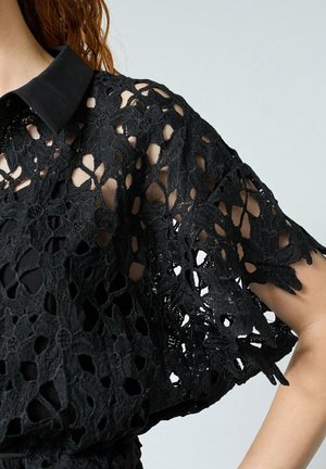 Sort hæklebluse med en ensfarvet sort krave, korte ærmer, intrikate blomster mønstre og åbne detaljer for åndbarhed.