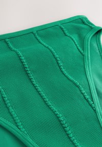 Zelené spodní díly bikiny z žebrované látky, s texturovaným povrchem a zakřivenými okraji s dekorativním prošitím podél švů.