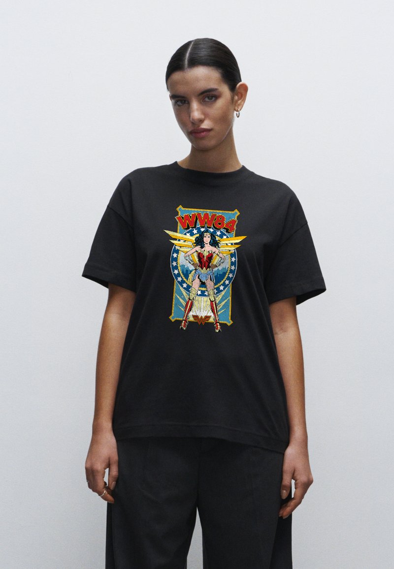 Camiseta de algodón negra con un gráfico colorido de Wonder Woman y el texto "WW84", sobre un diseño azul y amarillo con acentos de estrellas.