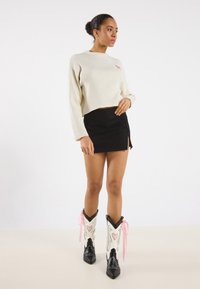 Pulover cropped cu dungi crem, fustă învelită neagră și cizme cowboy alb-negre cu accente roz în formă de inimă și panglici.