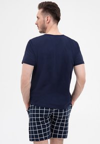 Granatowa koszulka z krótkimi rękawami, zestawiona z granatowo-białymi spodniami w kratkę. Gładka tekstura i luźny krój. Gładki widok z tyłu.