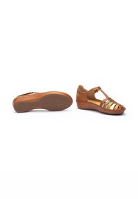 Sandalias de cuero marrón con puntera cerrada y diseño de tira en T. Presentan franjas metálicas y una suela de goma texturizada para mayor agarre.