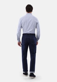 Herrenhemd mit langen Ärmeln in hellblau mit Streifen, kombiniert mit dunkelblauer Jeans. Das Hemd hat Knopfmanschetten; die Jeans haben eine gerade Passform mit aufgerollten Säumen.