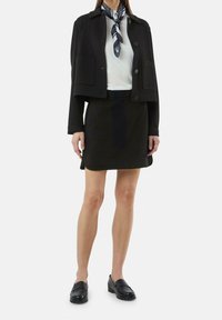 Czarna krótka kurtka z dwoma przednimi kieszeniami, biały prążkowany top i czarna spódnica. Czarne loafersy dopełniają outfit. Niebiesko-biała wzorzysta chusta.