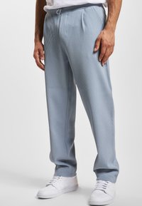 Pantalones de rayas en azul claro con cintura ajustable, que presentan pliegues frontales y un corte relajado, combinados con zapatillas blancas.