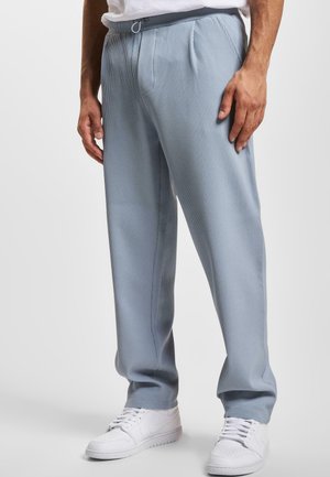 Light blue ribbed pants with a drawstring waist, featuring front pleats and a relaxed fit, paired with white sneakers.