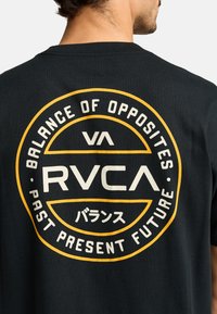 Schwarzes Baumwoll-T-Shirt mit einem runden Grafikdesign in Gelb und Weiß, das auf der Rückseite "RVCA", "Balance of Opposites" und japanischen Text zeigt.