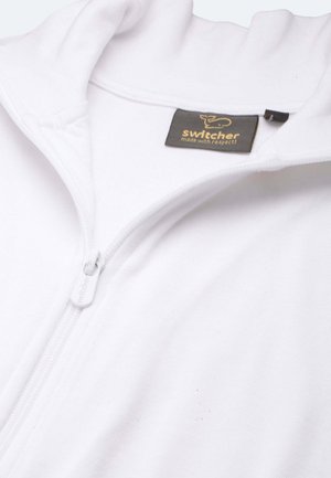 Felpa bianca con zip, in morbido tessuto, con colletto alto e un'etichetta con il logo "switcher" e un messaggio di sostenibilità. La zip è grigia.