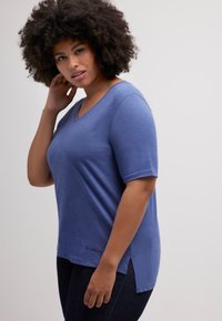 Blauwe V-hals t-shirt met korte mouwen, zachte textuur, zijslitsen en geborduurde details aan de zoom. Draag het met donkere spijkerbroeken.