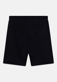 Pantalones cortos de algodón negro con cinturilla elástica, que cuentan con un bolsillo trasero y un pequeño logo cerca del bolsillo. Textura suave.