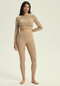 Beżowy krótki top z długim rękawem o prążkowanej strukturze, zestawiony z dopasowanymi leginsami o wysokim stanie, wszystko wykonane z miękkiego, elastycznego materiału.