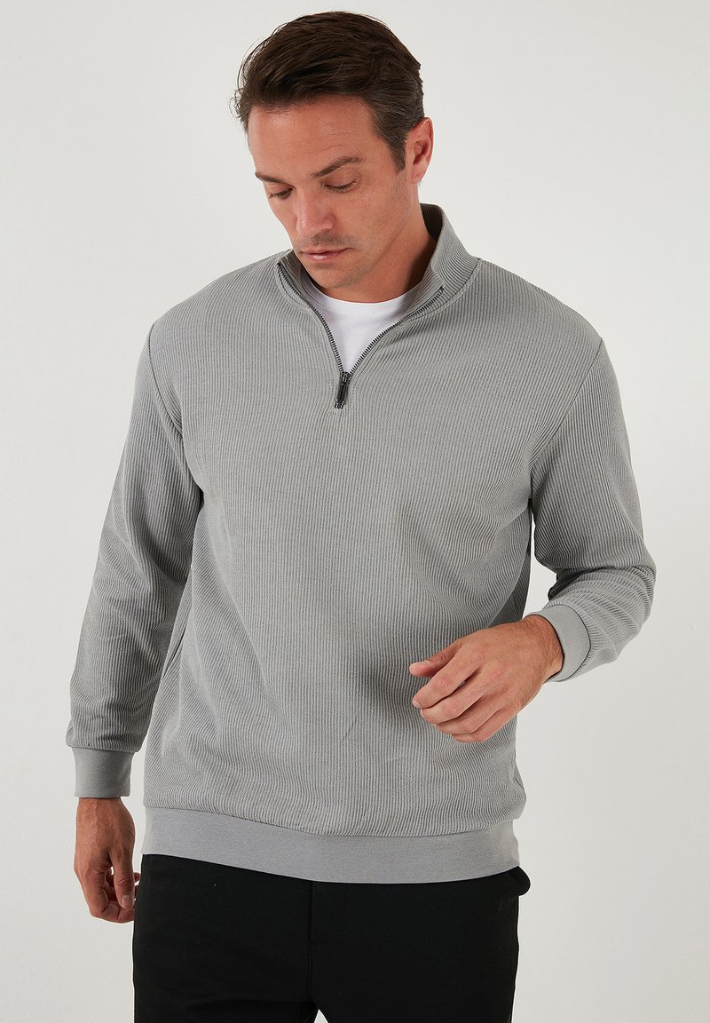 Gray pullover with a quarter-zip collar, ribbed texture, long sleeves, and a fitted waistband, worn over a white shirt.