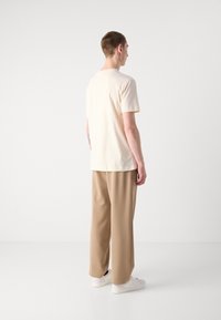 Crème kortekorte mouw t-shirt met een ontspannen pasvorm, gecombineerd met losse beige broeken en witte sneakers, gezien vanaf de achterkant.