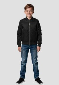 Bomber nero con chiusura frontale con zip, polsini e orlo a coste, abbinato a jeans blu e sneakers nere. Design casual e aderente.