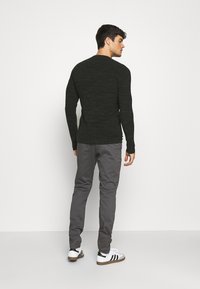 Suéter de manga larga verde oscuro con un patrón texturizado, combinado con pantalones gris ajustados y zapatillas blancas con rayas negras.
