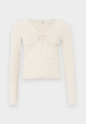Top de manga larga color crema elaborado en una suave tela texturizada. Presenta un escote en V y un detalle retorcido en el centro. Diseño cropped.