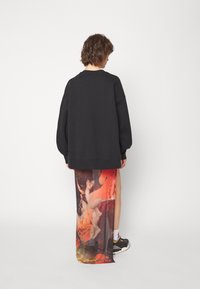 Suéter negro oversize con escote redondo, combinado con una falda larga transparente con estampado que presenta colores vibrantes e imágenes artísticas.